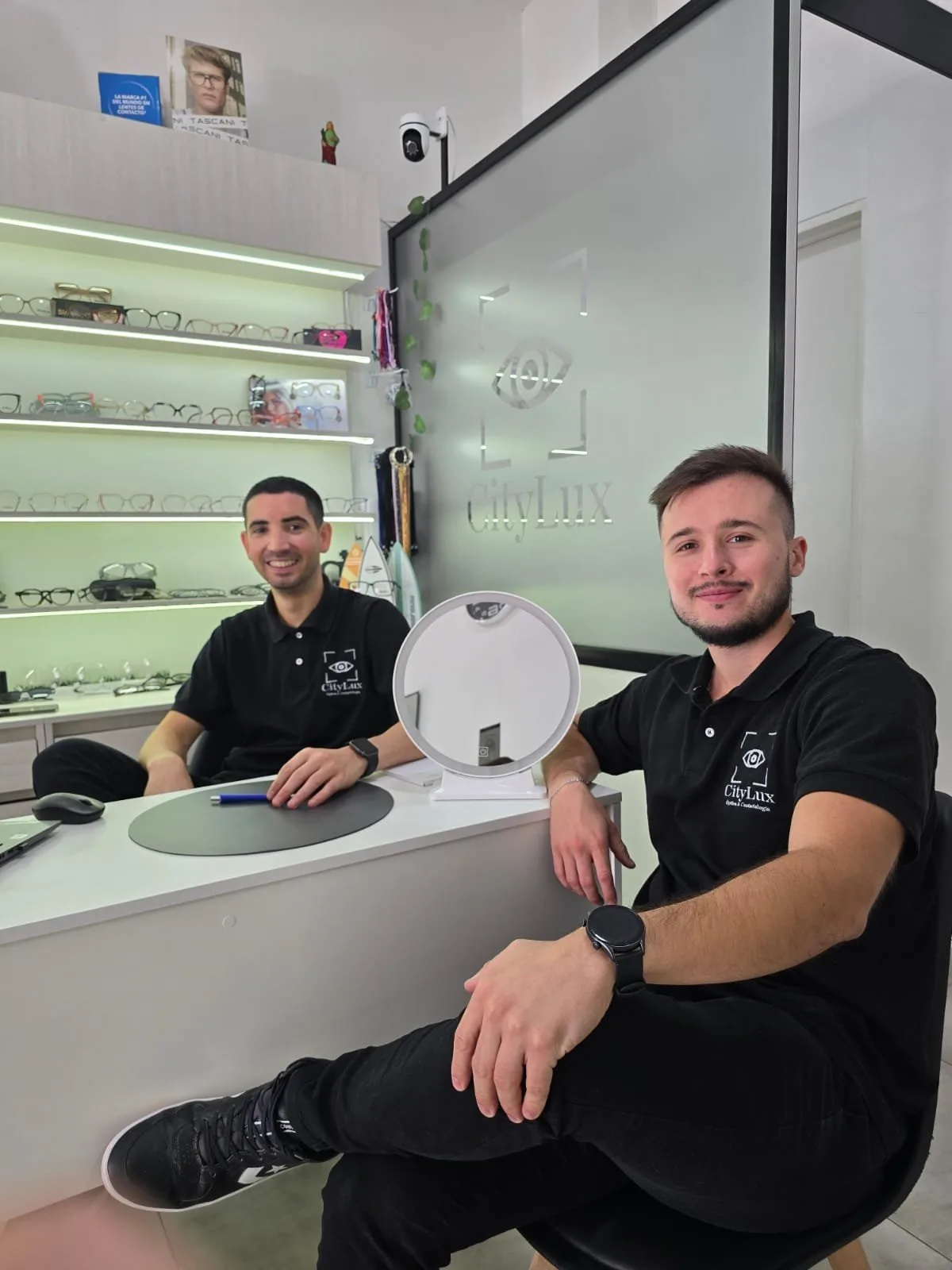 Los ópticos de CityLux sentados en el mostrador del local, con las vitrinas de armazones detrás